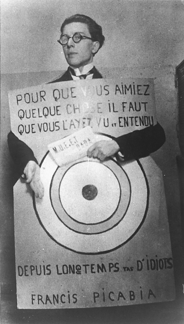 André Breton avec une pancarte Dada disant : Pour que vous aimiez quelque chose il faut que vous l'ayez vu et entendu depuis longtemps, tas d'idiots